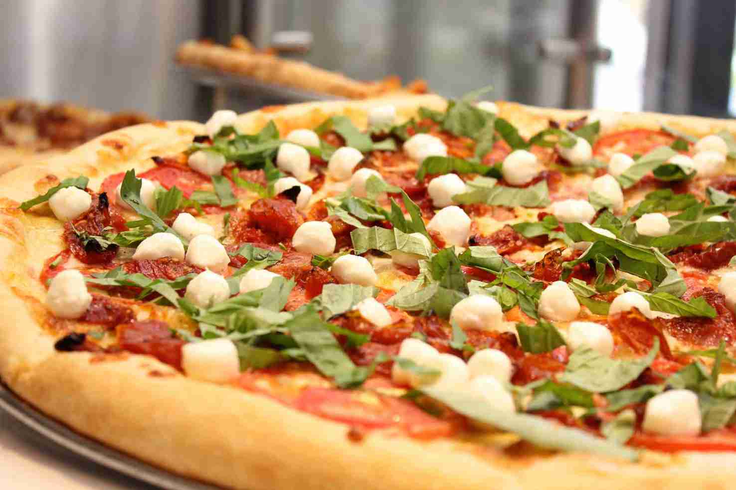 Close-up of a pizza topped with mozzarella balls, tomato slices, fresh basil leaves, and a crispy crust.