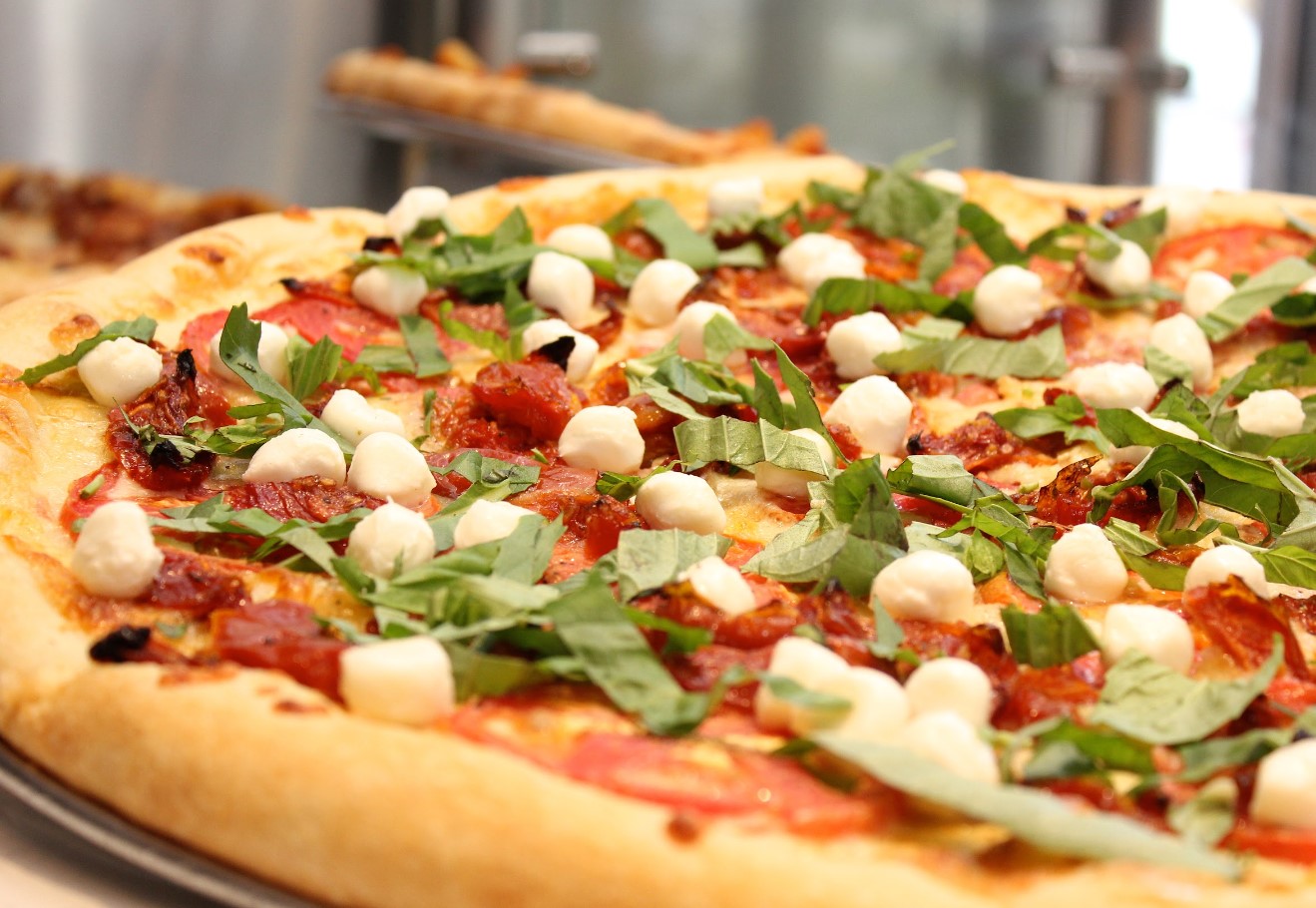 A close-up of a pizza topped with fresh basil leaves, tomato pieces, and small mozzarella balls on a golden-brown crust.