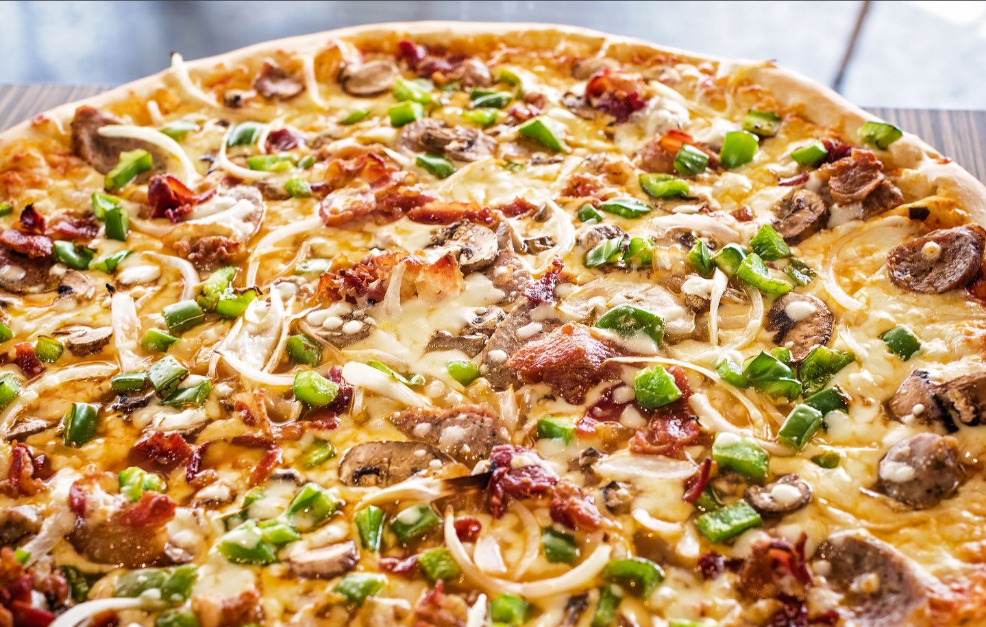 A close-up of a pizza topped with green bell peppers, onions, mushrooms, cheese, and pieces of bacon.