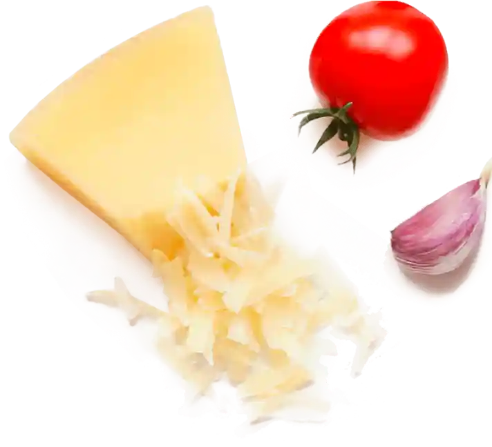 A wedge of cheese with grated pieces alongside a red tomato and a clove of garlic.